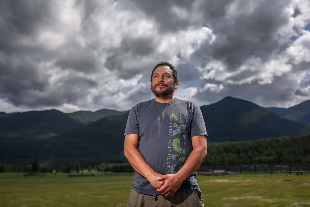 A photo of Jason Gravelle, the acting chief administrative officer of Yaq̓it ʔa·knuqⱡi’it, with a field and tree mountains behind him